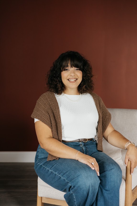 Stephanie smiling, seated in front of a deep red wall
